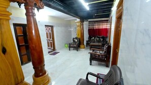 A spacious living area with a marble floor, wooden furniture, and a red curtain. - Kamath Homestay (Mavalli)