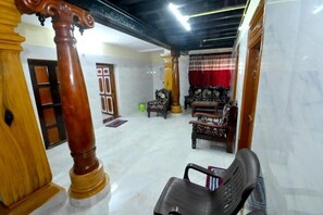 A spacious living area with a marble floor, wooden furniture, and a red curtain. - Kamath Homestay (Mavalli)