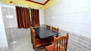 A dining area with a rectangular table surrounded by wooden chairs with cushioned seats. - Kamath Homestay (Mavalli)