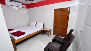 A bedroom with a bed, a wooden door, a bench, and an air conditioning unit. - Kamath Homestay (Mavalli)