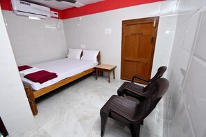 A bedroom with a bed, a wooden door, a bench, and an air conditioning unit. - Kamath Homestay (Mavalli)
