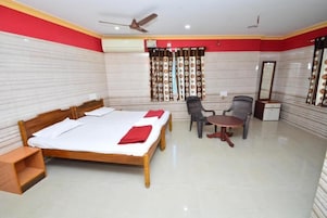 Habitación de hotel con cama, una mesita, una silla, ventilador de techo y ventana con cortinas.