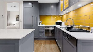 A modern kitchen with grey cabinets, a yellow backsplash, stainless steel appliances, and a white countertop. - Spacious 3-Bed Apartment in Melbourne CBD (Melbourne)