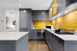 A modern kitchen with grey cabinets, a yellow backsplash, stainless steel appliances, and a white countertop. - Spacious 3-Bed Apartment in Melbourne CBD (Melbourne)