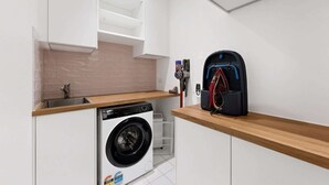 A compact laundry room with a washing machine, a drying rack, and a vacuum cleaner. - Spacious 3-Bed Apartment in Melbourne CBD (Melbourne)
