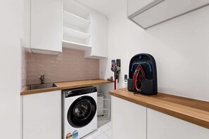 A compact laundry room with a washing machine, a drying rack, and a vacuum cleaner. - Spacious 3-Bed Apartment in Melbourne CBD (Melbourne)