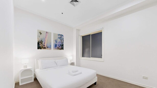 A bedroom with a bed, two bedside tables, a window, and two wall-mounted paintings. - Spacious 3-Bed Apartment in Melbourne CBD (Melbourne)