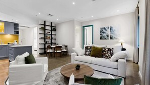 A modern living room with a white sofa, a coffee table, and a dining area with chairs. - Spacious 3-Bed Apartment in Melbourne CBD (Melbourne)