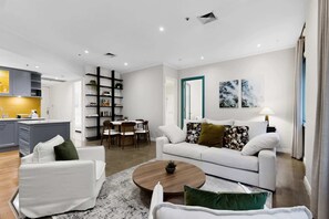 A modern living room with a white sofa, a coffee table, and a dining area with chairs. - Spacious 3-Bed Apartment in Melbourne CBD (Melbourne)