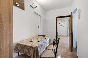 Ein Essbereich mit einem für zwei Personen gedecktem Tisch, einer Tür zu einem anderen Raum und einer an der Wand befestigten Leuchte.