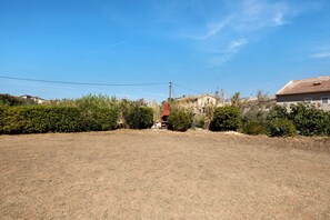 Paisaje rural con cielo despejado, hierba seca y algunos edificios al fondo.