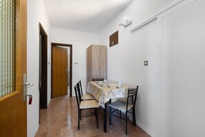 A dining area with a table set for two, chairs, a cabinet, and a door. - Apartment 'Volarić Pag' with Sea View, Balcony and Air Conditioning (Pag)