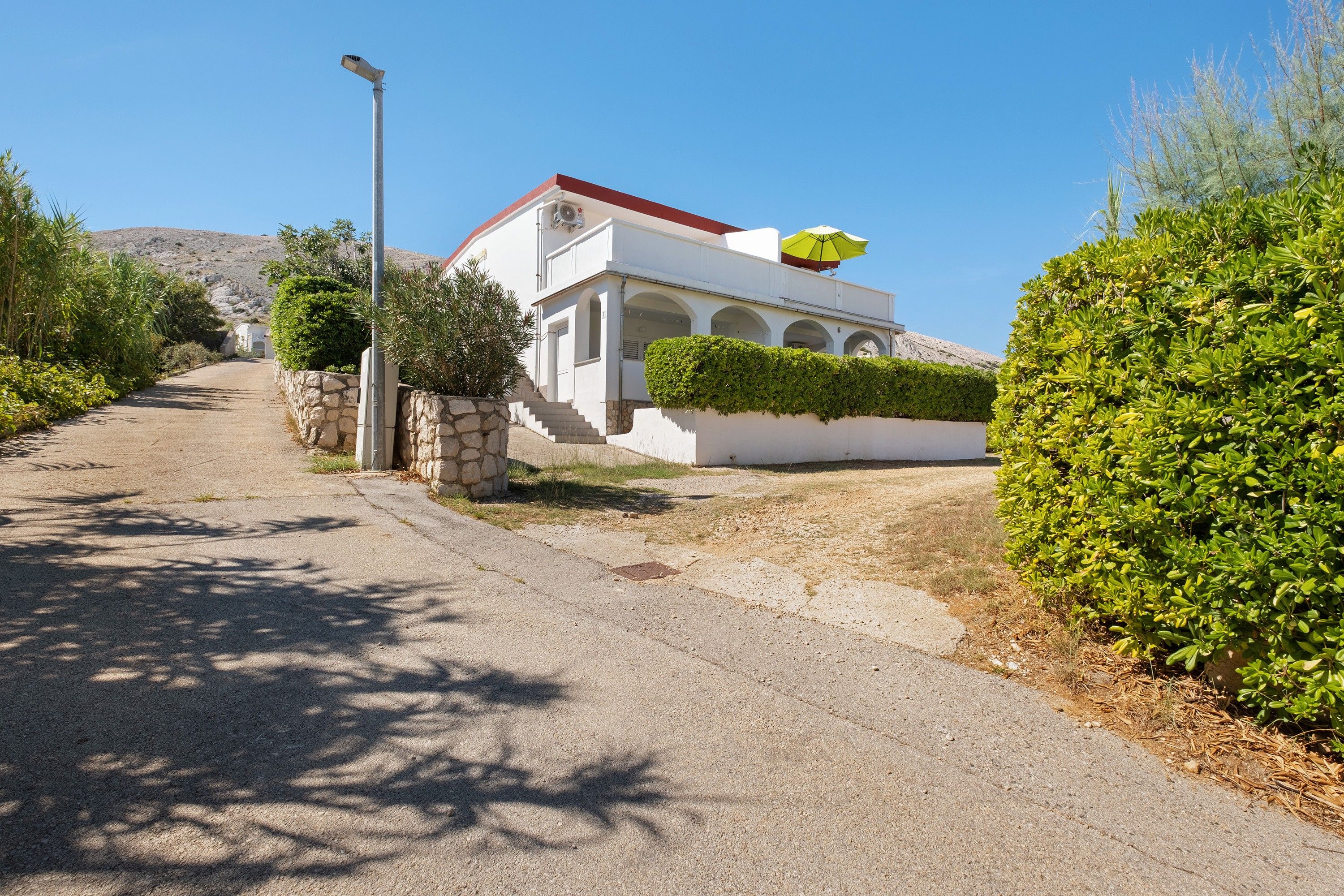 A white building with a red roof, a stone wall, and a yellow umbrella.