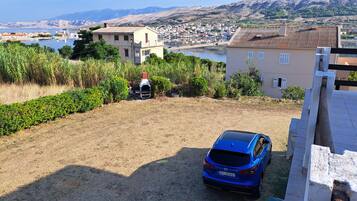 A blue car parked in a driveway with a view of a lake and buildings in the background.