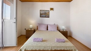 A bedroom with a wooden ceiling, a bed with a quilted bedspread, two nightstands with lamps, and a painting on the wall. - Apartment 'Volarić Pag' with Sea View, Balcony and Air Conditioning (Pag)