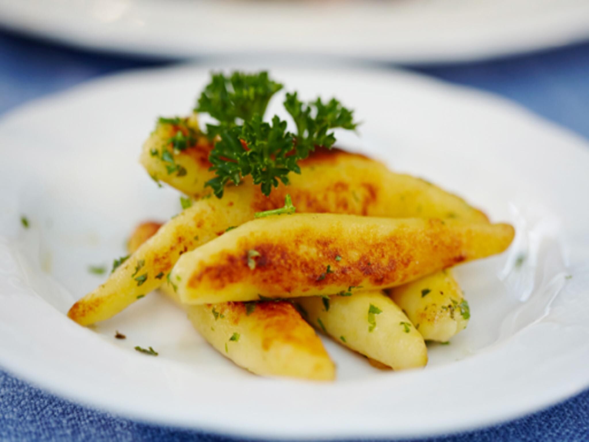 Een bord met goudbruine aardappelpartjes, versierd met peterselie.