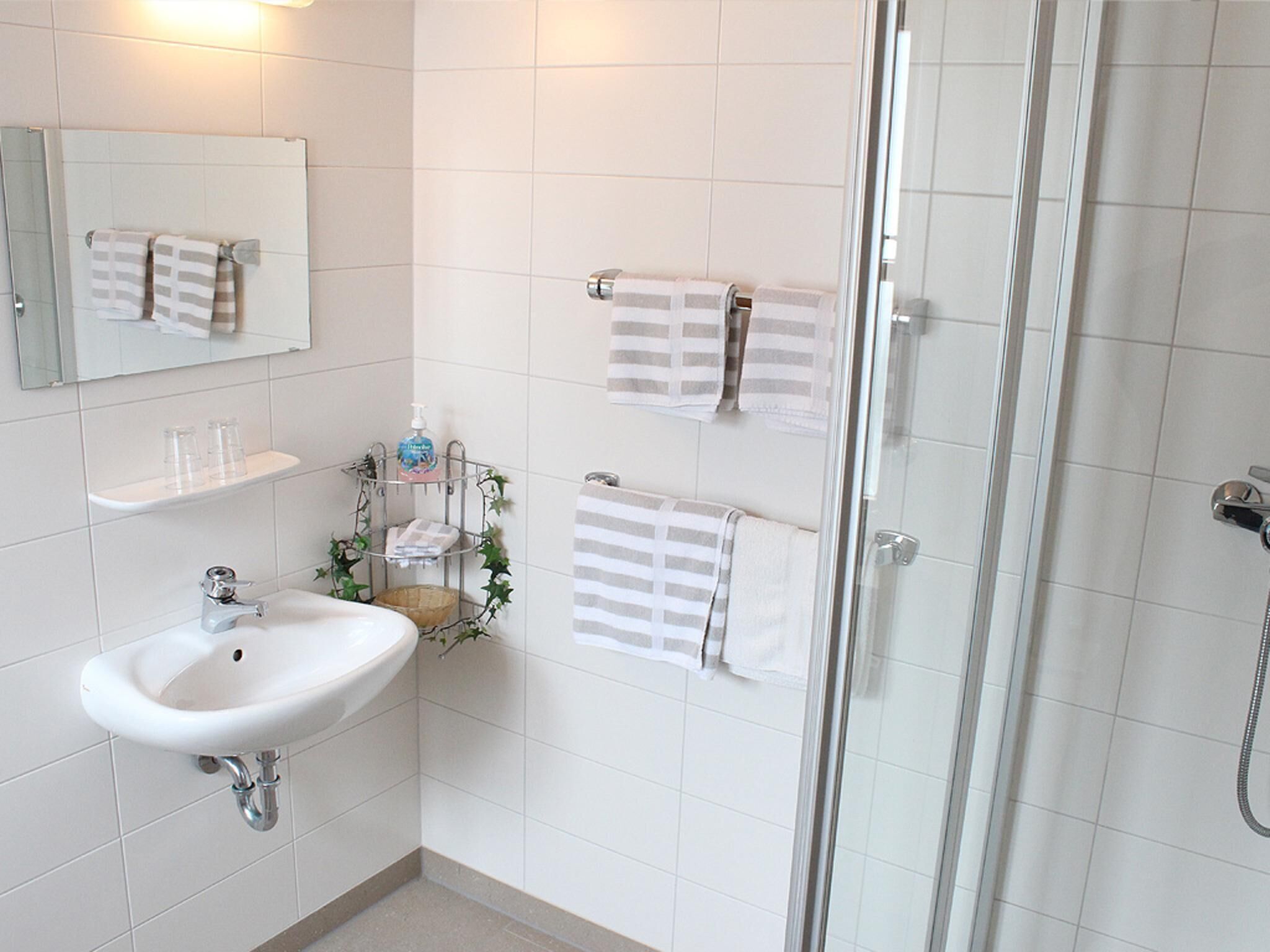 A bathroom with a sink, mirror, towel rack, and shower.