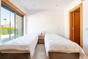 Ein Schlafzimmer mit zwei Betten, einem Nachttisch und einem Fenster mit Blick auf Grünflächen.