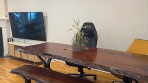 Uma mesa de conferência com bancos, uma planta em vaso e uma televisão na parede.
