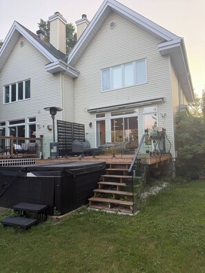 A two-story house with a deck, outdoor seating, and a hot tub. - Waterfront Escape with Private Hot Tub & Terrace (Laval)