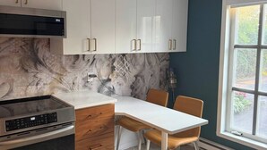 Cozinha moderna com armários brancos, forno embutido e área de jantar com mesa e cadeiras.
