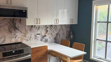 A modern kitchen with white cabinets, a built-in oven, and a dining area with a table and chairs.