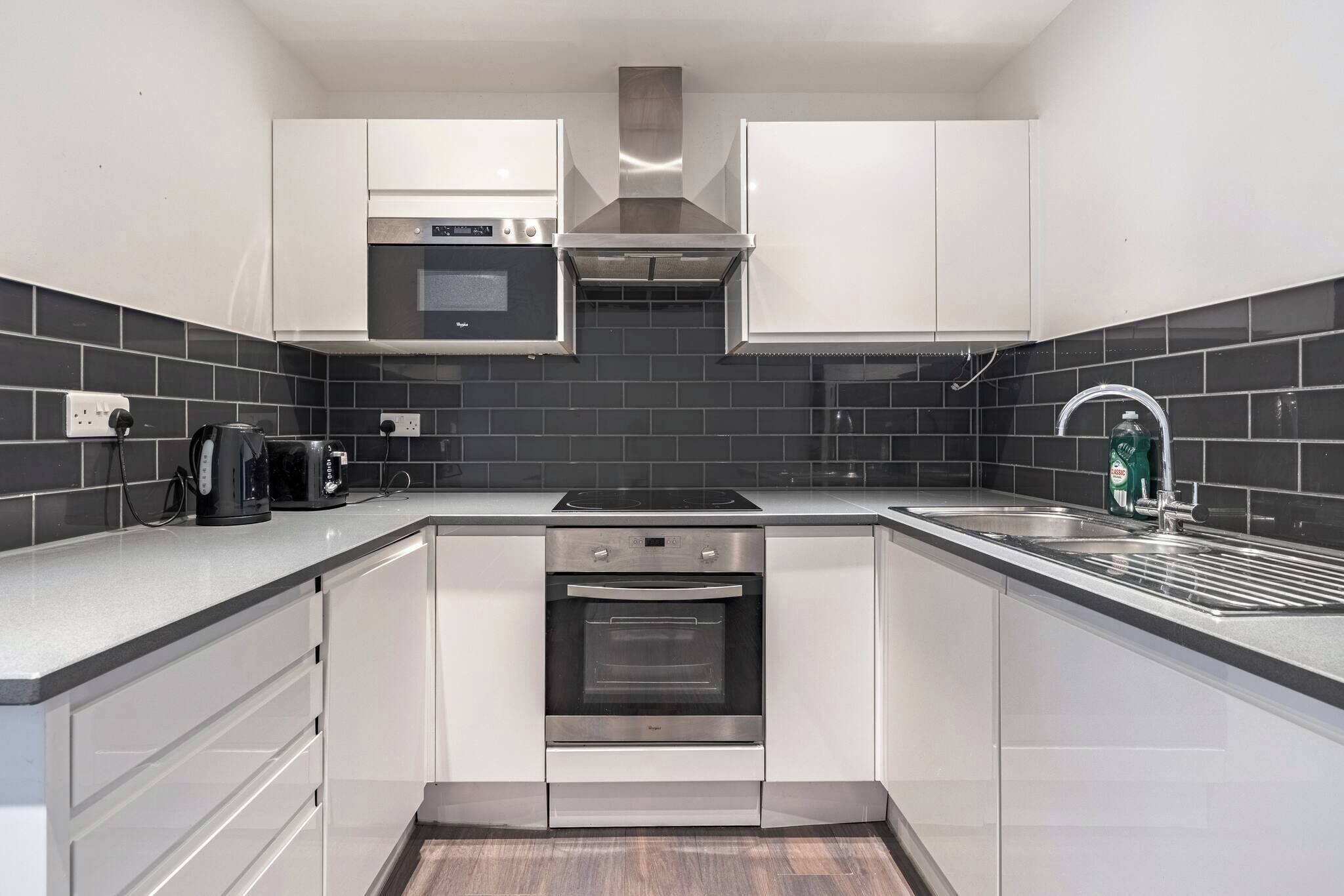 Een moderne keuken met witte kasten, een ingebouwde oven, een magnetron en een roestvrijstalen afzuigkap.