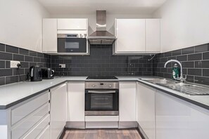 A modern kitchen with white cabinets, a built-in oven, a microwave, and a stainless steel range hood. - Spacious Wimbledon Flat Walk to Staton Sleeps 4 (London)