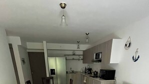 En kompakt opholdsstue med spiseplads, tekøkken og sofa.