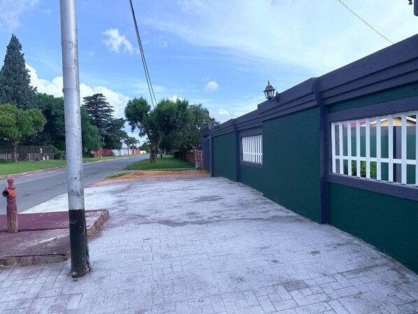 A paved sidewalk adjacent to a building with a green exterior and white window bars.