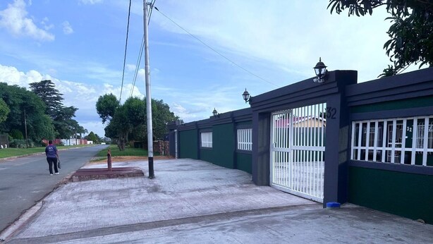 Un ingresso recintato con un cancello in metallo e un viale di cemento che conduce a un edificio.