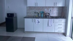 Una cucina compatta con mobili bianchi, un piano di lavoro, una macchina del caffè e un forno a microonde.