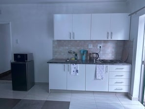 Eine kleine Küche mit weißen Schränken, einer Arbeitsplatte, einer Kaffeemaschine und einer Mikrowelle.