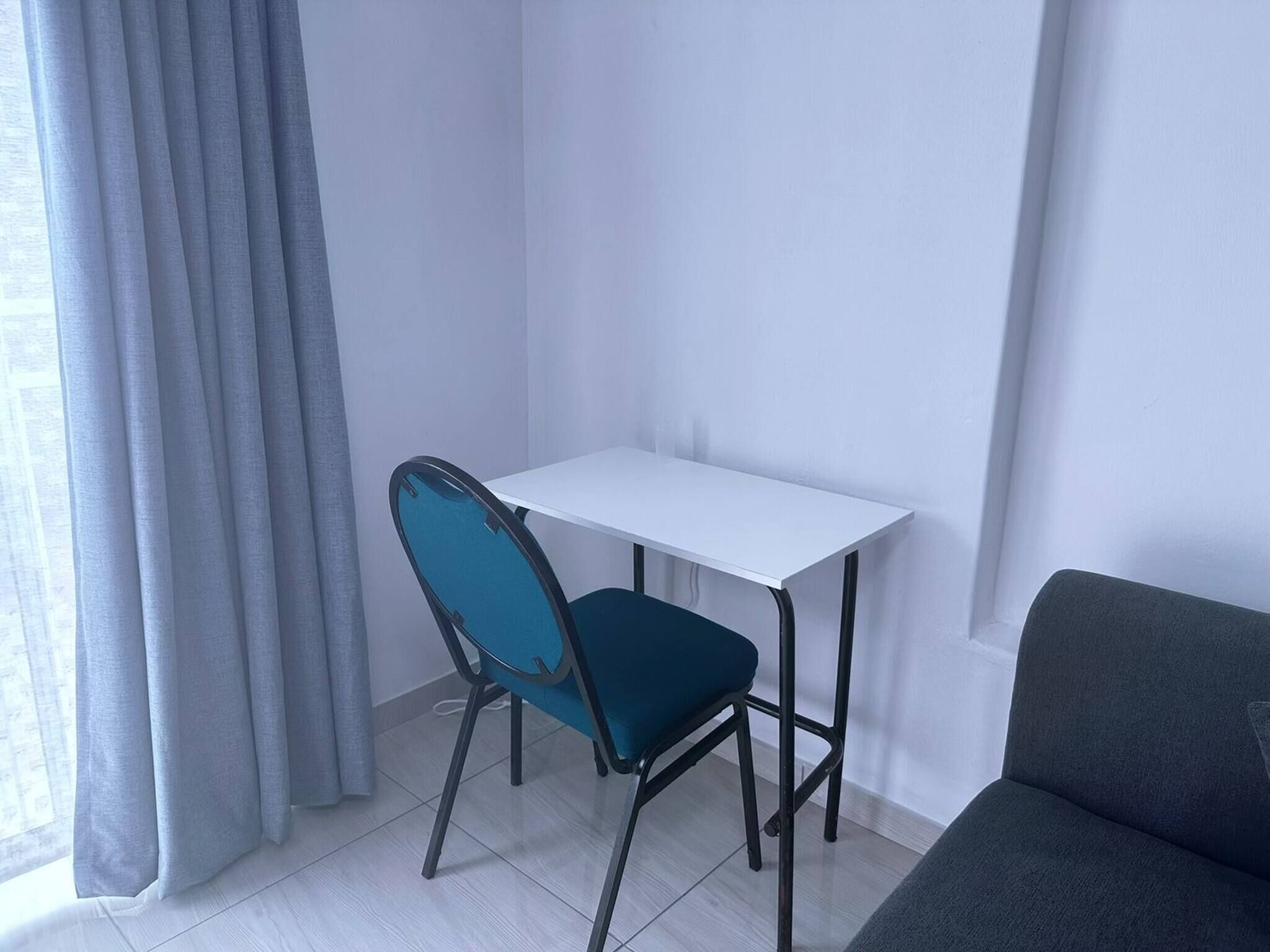A small, clean room with a white desk, a blue chair, and a grey sofa.