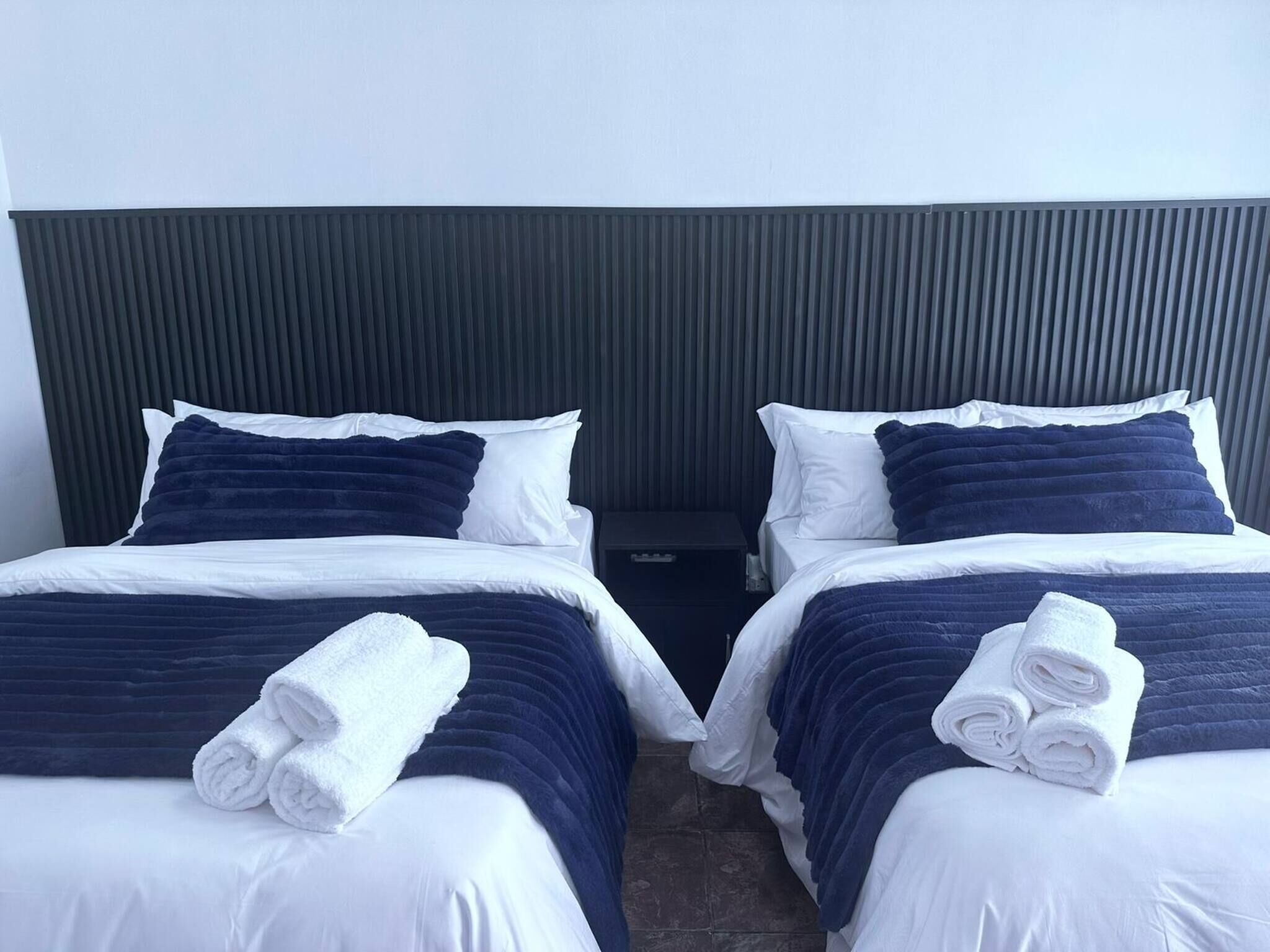 Two twin beds with dark blue bedding and white pillows, each with a rolled white towel on the footboard.