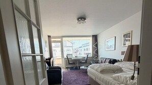 A hotel room with a bed, a desk, a chair, and a window with a view of buildings. - Strandstraße Building, Apartment 33 (Sylt)