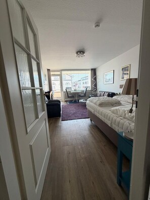 A hotel room with a bed, a desk, a chair, and a window with a view of buildings. - Strandstraße Building, Apartment 33 (Sylt)