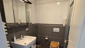 A bathroom with a white sink, mirror, and wooden toilet. - Strandstraße Building, Apartment 33 (Sylt)