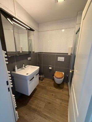A bathroom with a white sink, mirror, and wooden toilet. - Strandstraße Building, Apartment 33 (Sylt)