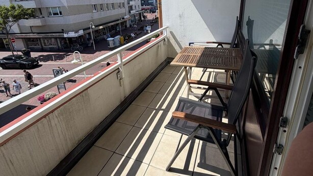 A balcony with a table and chairs, a view of a city street, and a building with multiple floors. - Strandstraße Building, Apartment 33 (Sylt)