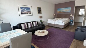 A modern, well-lit living room with a sofa, a bed, a coffee table, and a desk. - Strandstraße Building, Apartment 33 (Sylt)