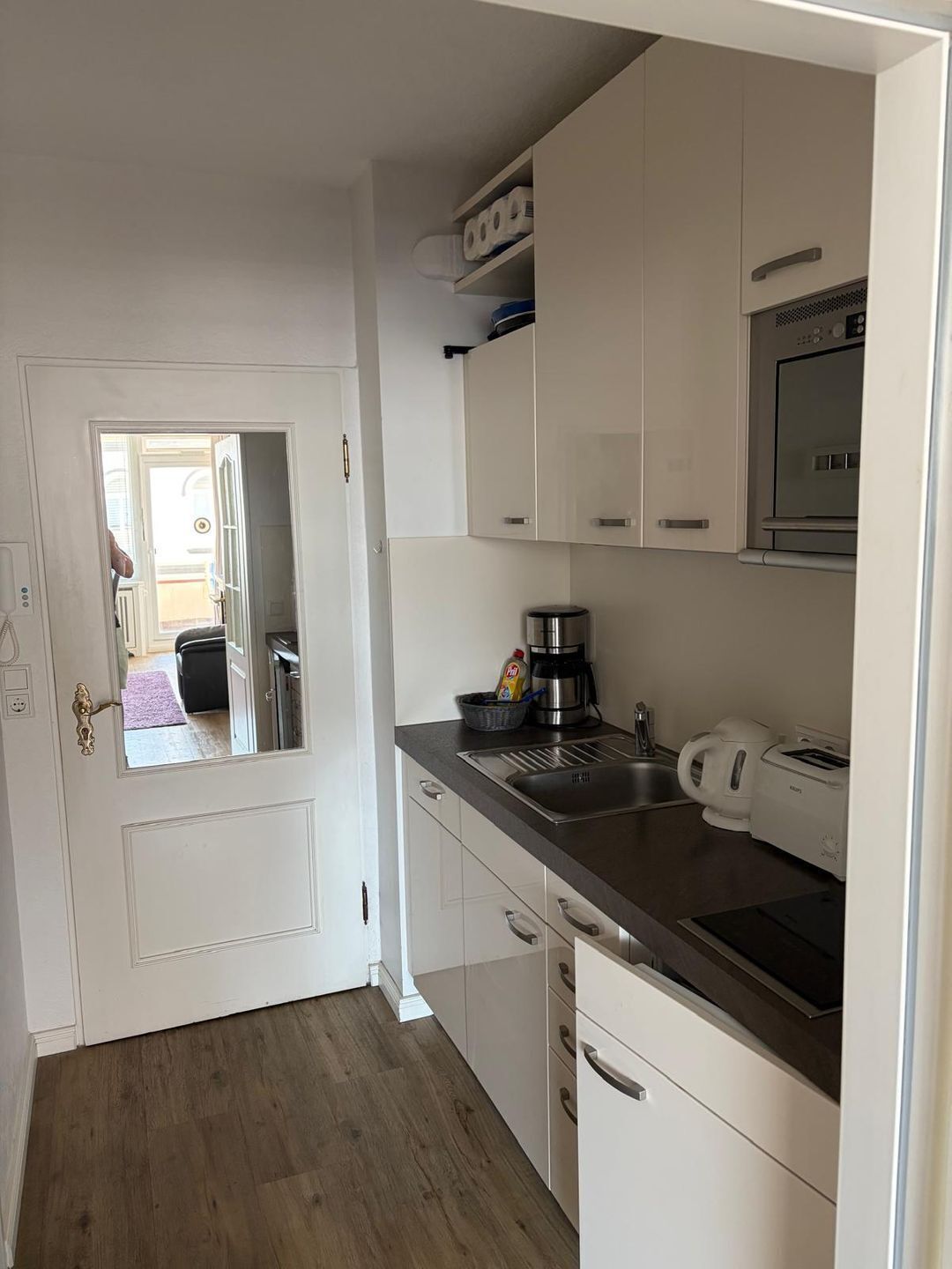 A compact kitchen with white cabinets, a stainless steel sink, a coffee maker, and a toaster.