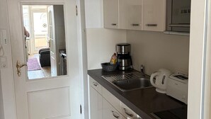 A compact kitchen with white cabinets, a stainless steel sink, a coffee maker, and a toaster. - Strandstraße Building, Apartment 33 (Sylt)