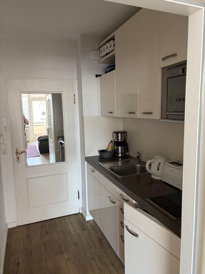 A compact kitchen with white cabinets, a stainless steel sink, a coffee maker, and a toaster. - Strandstraße Building, Apartment 33 (Sylt)