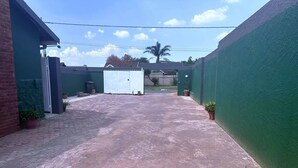 Un cortile pavimentato con un cancello bianco, piante in vaso e un muro verde.