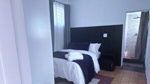 Una camera d'albergo con un letto, un tavolino, una panca e un angolo doccia.
