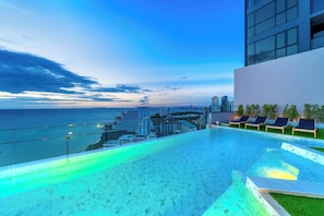 Ein Pool ohne Rand mit Blick auf die Stadt, Liegestühle und ein modernes Gebäude.