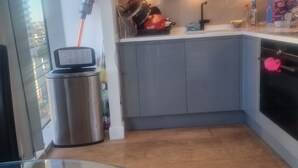 A compact kitchen with a stainless steel trash bin, a small refrigerator, and a microwave. - Canary wharf view apartment (London)