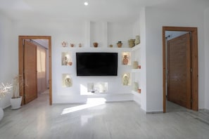 Een ruime kamer met een flatscreen-tv aan de muur, houten deuren en een reeks planken met keramiek.