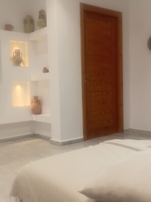 A room with a bed, a wooden door, and shelves with decorative items. - Charming 3-Bedroom Apartment in Historic Carthage, Tunisia (Site archéologique de Carthage)